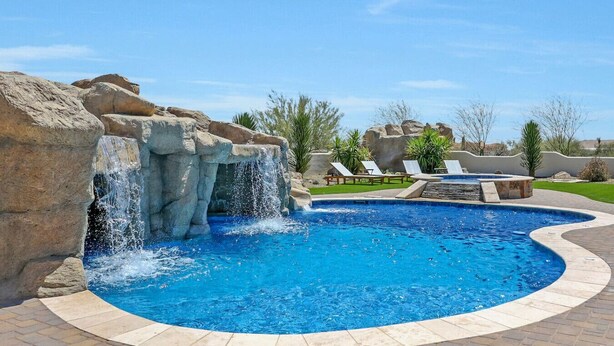 A swimming pool with a waterfall feature, surrounded by lounge chairs and a landscaped garden.