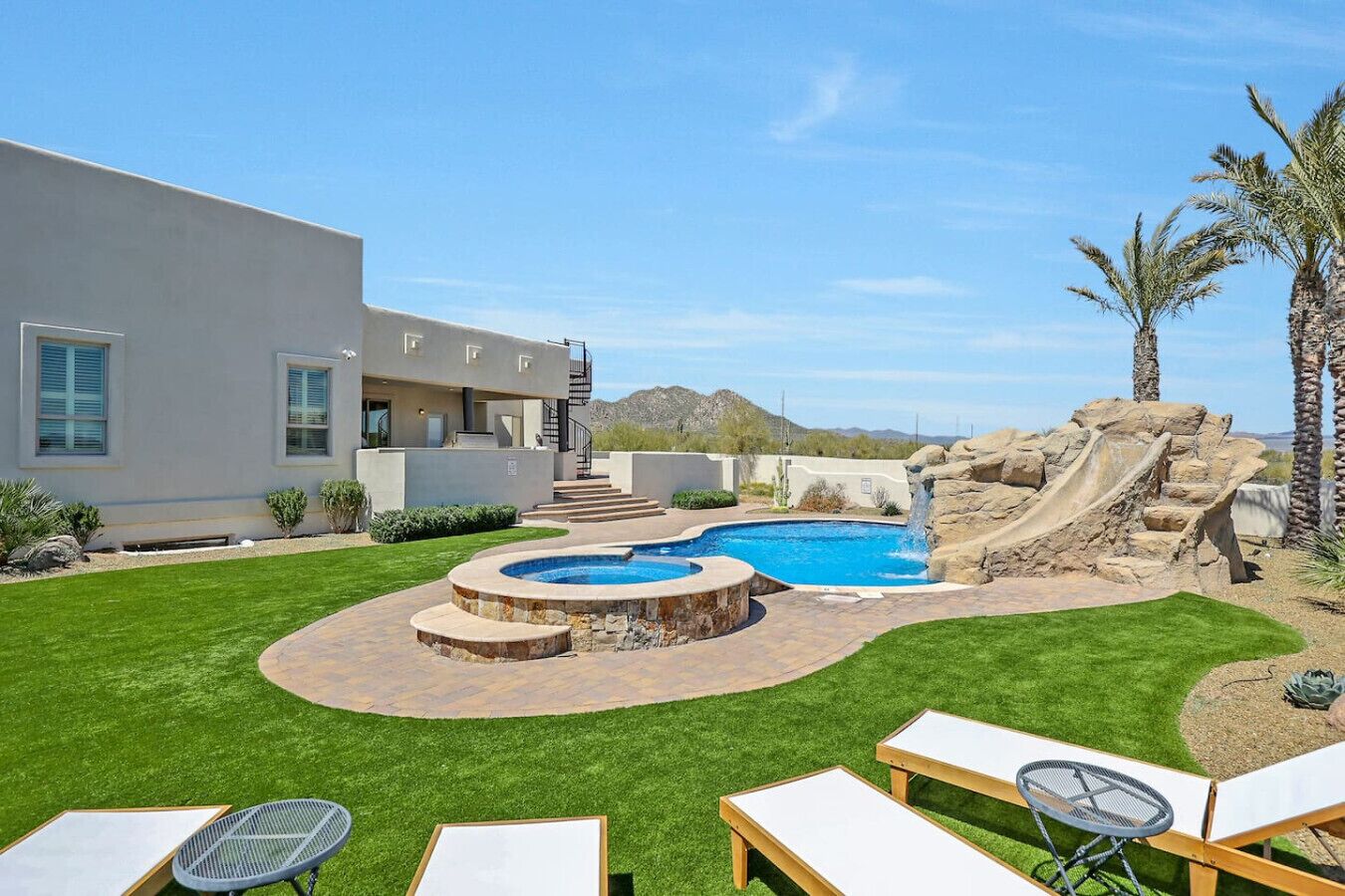 A modern house with a swimming pool, a rock waterfall, and a well-maintained lawn.