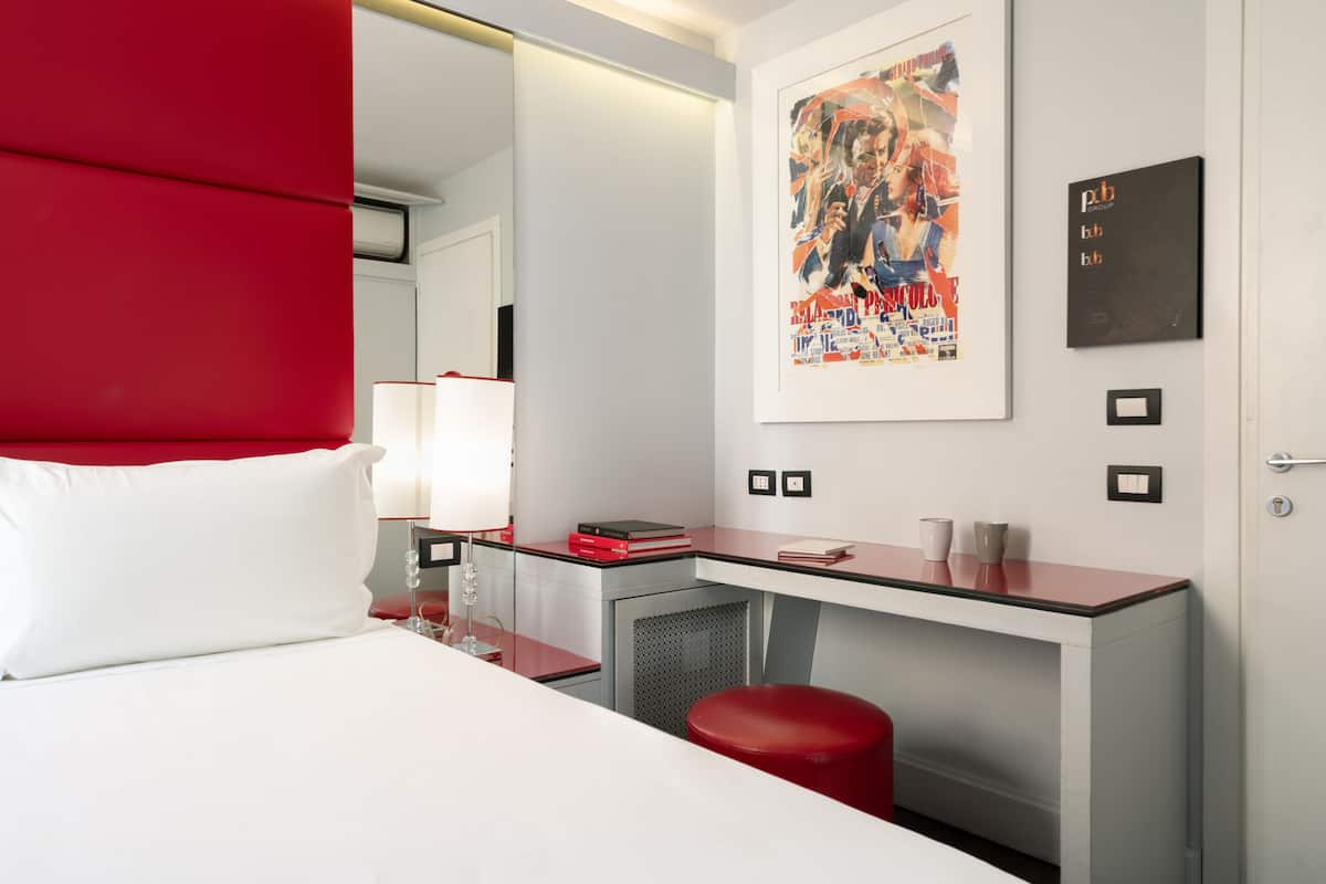 Una habitación de hotel moderna con cama, escritorio y una pared de acento roja.