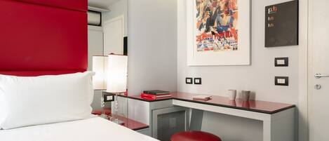A modern hotel room with a bed, a desk, and a red accent wall.