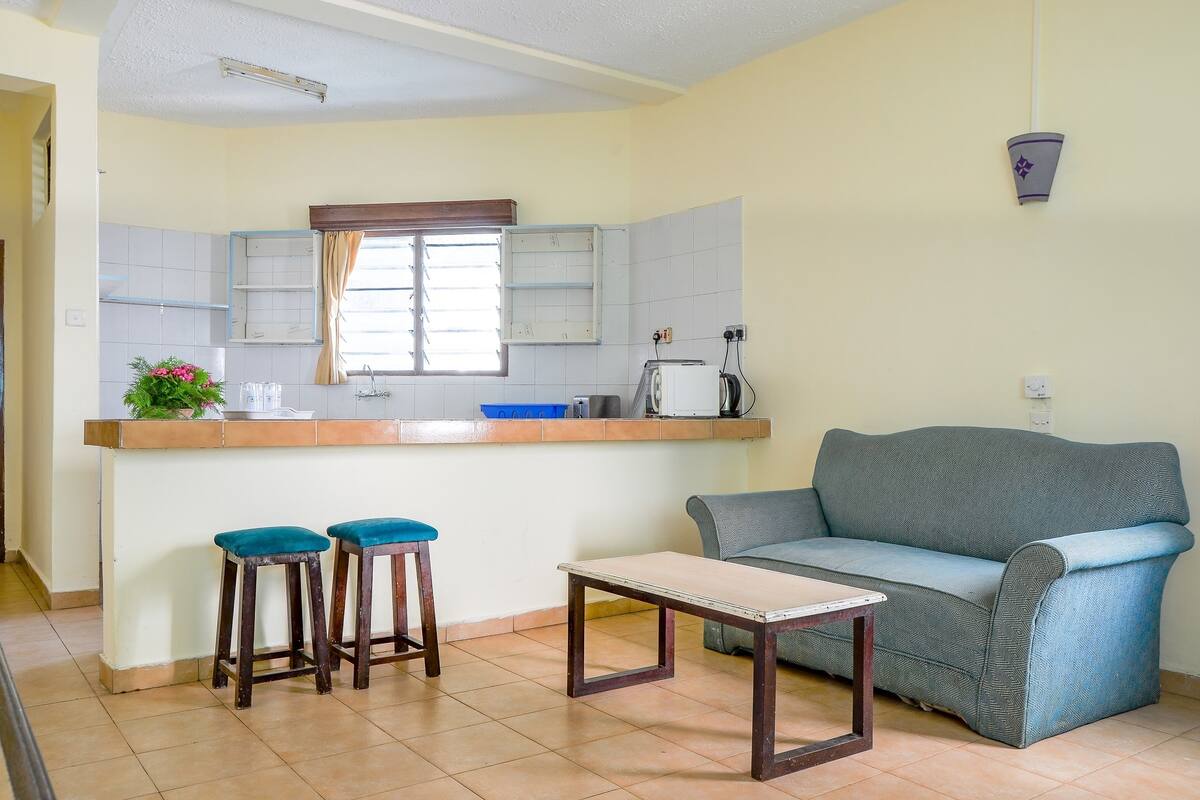 A compact living space with a kitchenette, a sofa, two stools, and a small table.