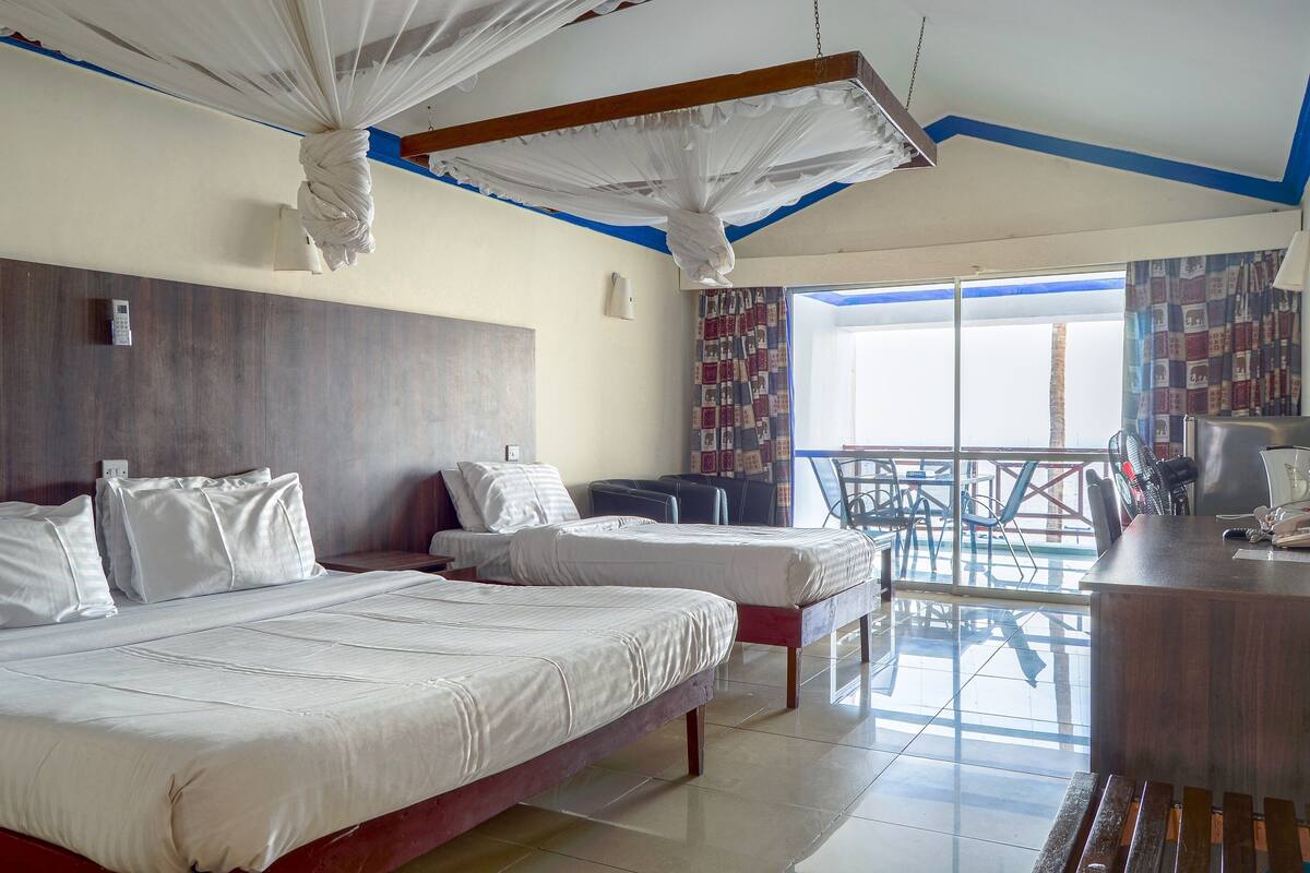 A hotel room with two beds, a balcony with a view, and a desk with a chair.