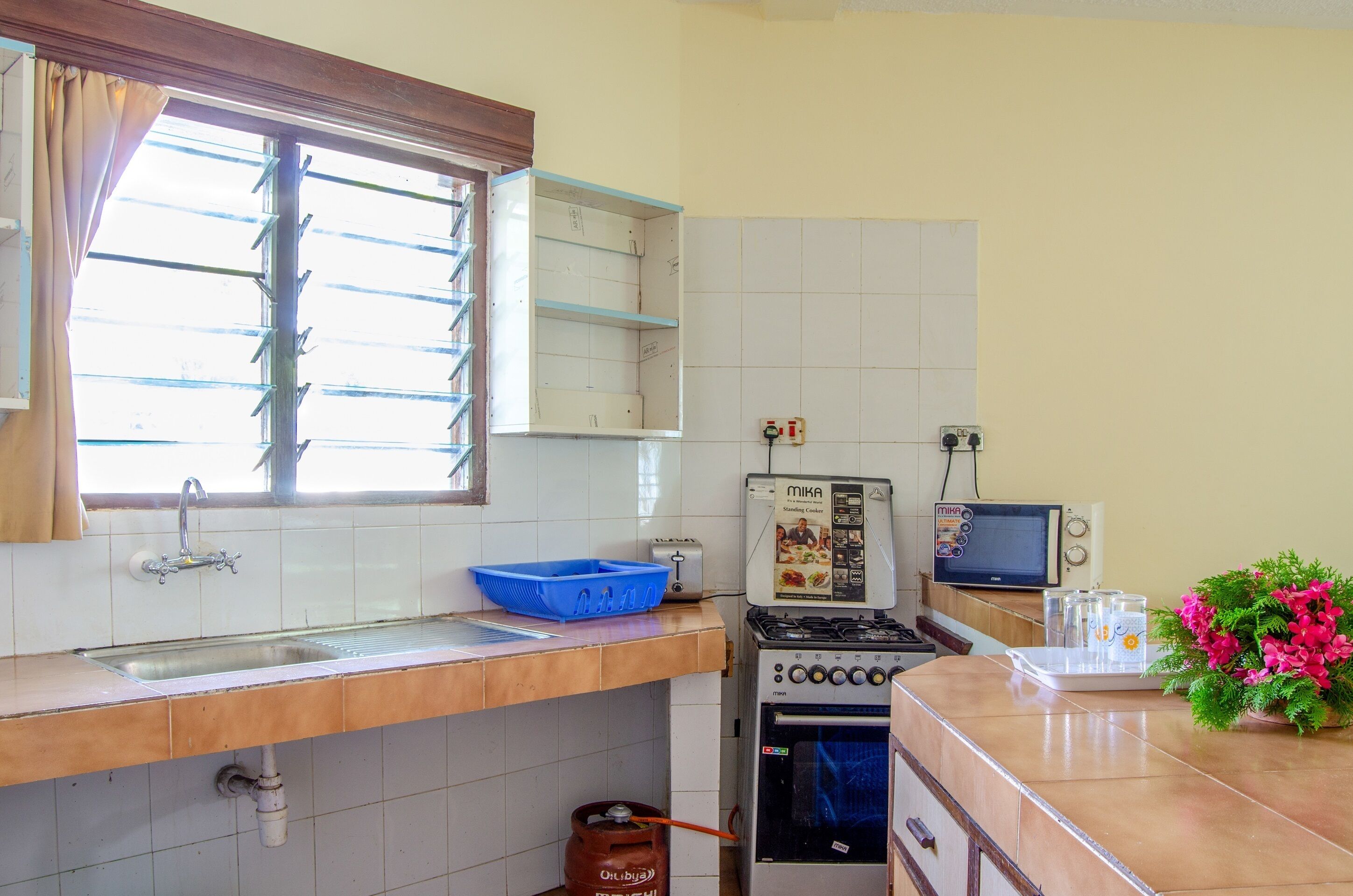 A kitchen with a sink, stove, microwave, and a window with a curtain.