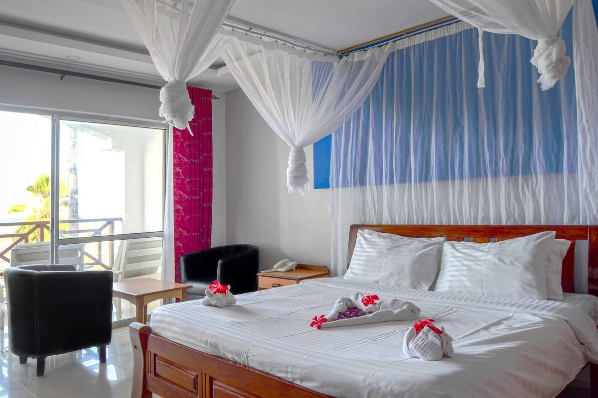 A hotel room with a bed, a bedside table, a chair, and a balcony with a view.
