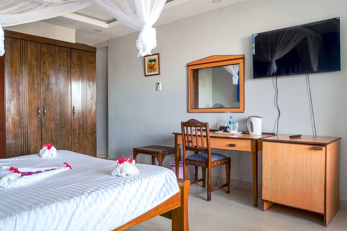 A hotel room with a bed, wooden wardrobe, desk, chair, and a television.