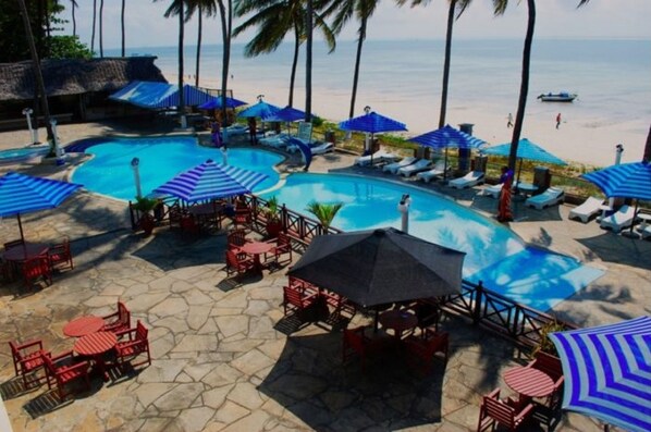 Un espace piscine avec des chaises longues et des parasols, une terrasse en pierre et une vue sur la plage.