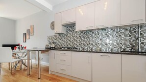 Ett modernt kök med vita skåp, kakel ovanför arbetsbänken och en matplats med ett glasbord och stolar.