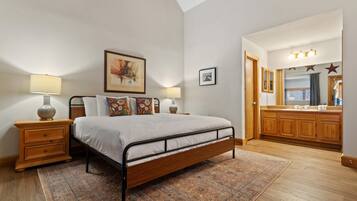 Un dormitorio con cama, mesitas de noche, una alfombra, un cuadro, un espejo y armarios de madera.