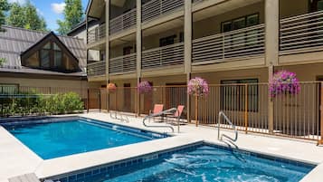 Uma piscina com hidromassagem, rodeada por um edifício de vários andares com varandas e grades.