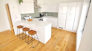 A modern kitchen with white cabinetry, a central island with stools, and a green-tiled backsplash.