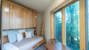 A cozy room with a wooden bed, a small table, and a window with a forest view. - Charming Studio W Kitchenette, Hot Tub Near River Condo by RedAwning (Telluride)