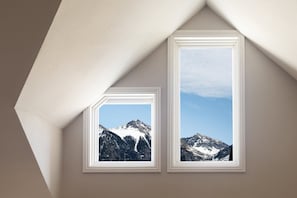 Une pièce dotée de deux fenêtres, chacune encadrée de blanc, donnant sur un paysage montagneux.