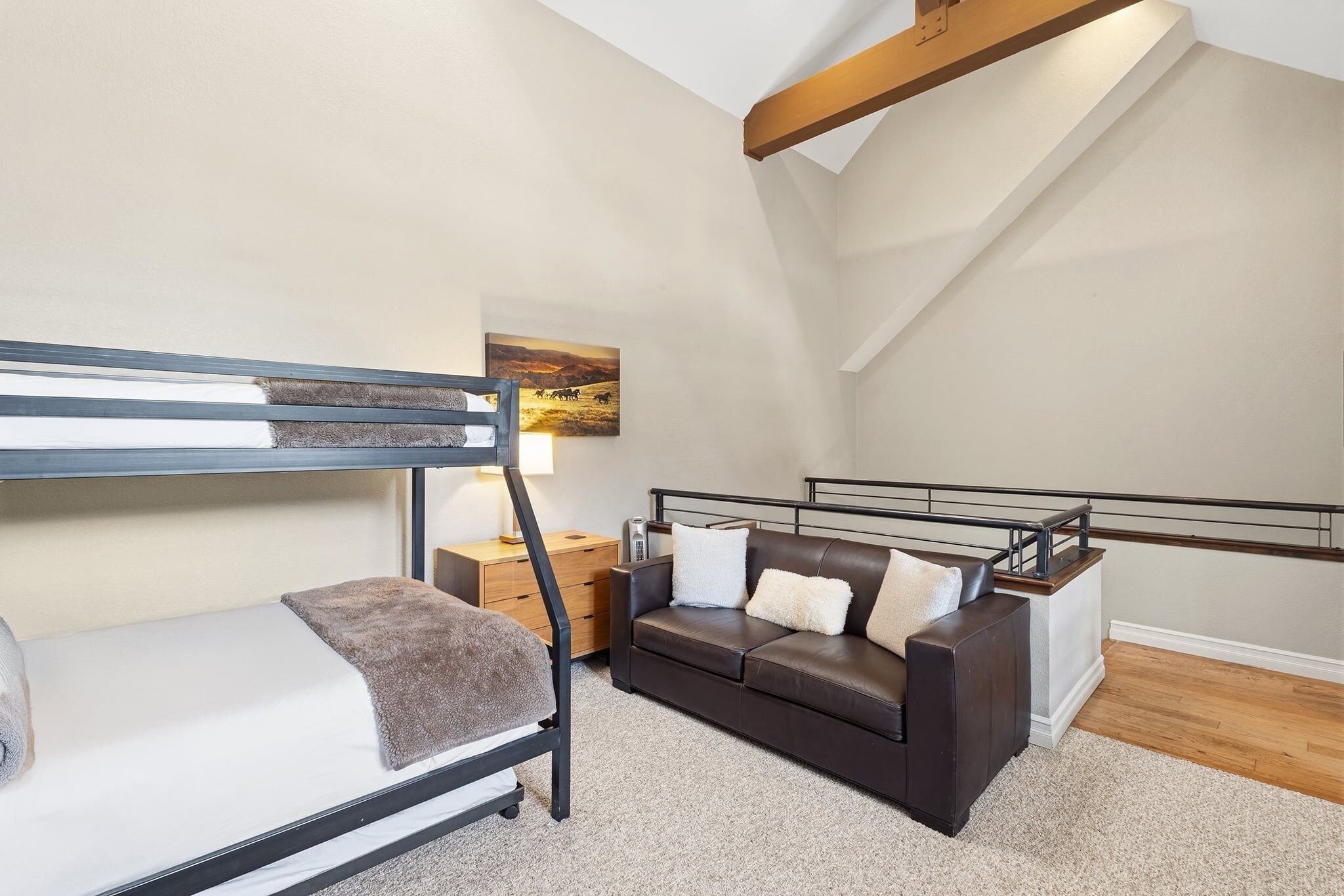 A bedroom with a bunk bed, a sofa, a nightstand, and a painting on the wall.