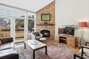 A living room with a stone fireplace, a television, and a view of mountains through large windows. - Slopeside Paradise Penthouse At Lift 7, Views, Fireplace, Deck, Hot Tub 3 Bedroom Condo by RedAwning (Telluride)