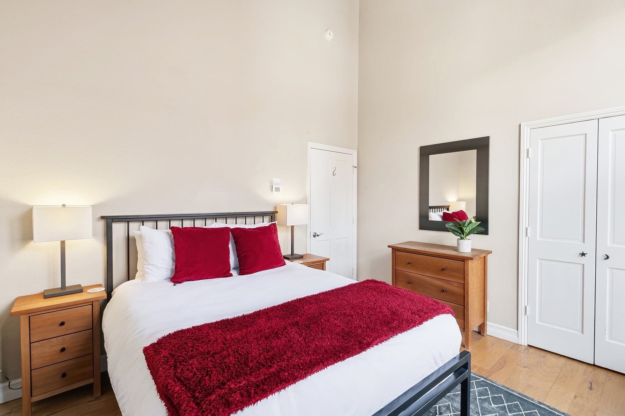 A neatly arranged bedroom with a bed, bedside tables, a dresser, a mirror, and a wardrobe.