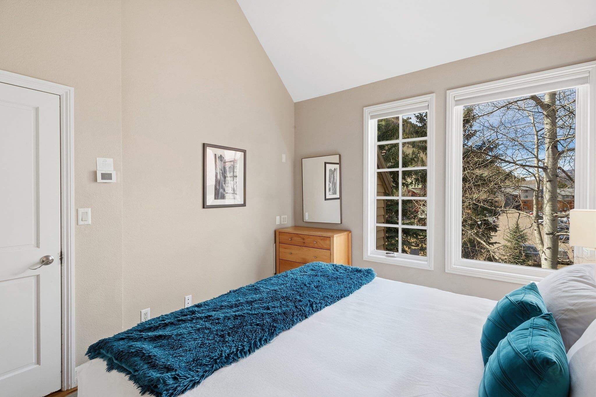 A bedroom with a bed, a dresser, a window with a view, and a door.