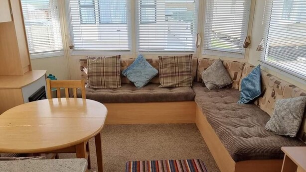 A compact RV interior with a dining area, a sofa with cushions, and a striped rug. - Beautiful 2-bed Caravan in Abergele Town (Abergele)