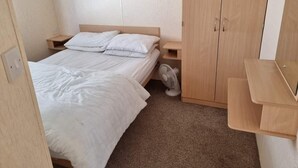 A small, neatly arranged bedroom with a single bed, a nightstand, a wardrobe, and a fan. - Beautiful 2-bed Caravan in Abergele Town (Abergele)