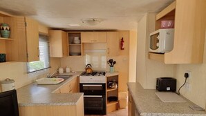 A compact kitchen with wooden cabinets, a gas stove, a microwave, and a toaster. - Beautiful 2-bed Caravan in Abergele Town (Abergele)