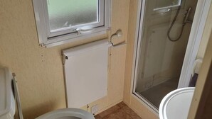 A small bathroom with a toilet, a window, and a shower. - Beautiful 2-bed Caravan in Abergele Town (Abergele)