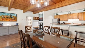 A modern kitchen with wooden cabinets, a stainless steel refrigerator, and a dining area with a glass table and wooden chairs. - Riverside Dream! Quiet Spot W Deck, 5 Min Walk To Gondola & Main St. 2 Bedroom Condo by RedAwning (Telluride)