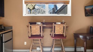 A kitchen with two wooden stools, a window with a view of a snowy mountain, and a small table with a vase. - Ski Trip Value! Walk Everywhere, Hot Tub, Top Floor 1 Bedroom Condo by RedAwning (Telluride)