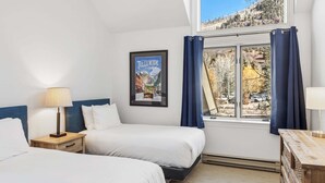 A hotel room with two beds, a window with curtains, a framed picture on the wall, and a lamp on the nightstand. - Lift 7 Ski In/out Hot Tub, Ski Locker, Garage Parking + Shuttle To Gondola 2 Bedroom Condo by RedAwning (Telluride)