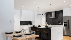 Uma cozinha moderna com armários brancos, uma ilha central com bancos, uma geladeira de aço inoxidável e uma backsplash preta.