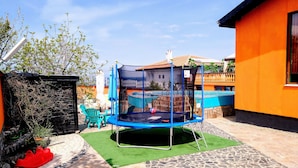 A backyard with a trampoline, green artificial turf, and a stone patio. - Sea Marble Villa Studio (Sozopol)