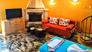 A living room with a fireplace, a sofa, a glass coffee table, and a TV on a wooden cabinet. - Sea Marble Villa Studio (Sozopol)