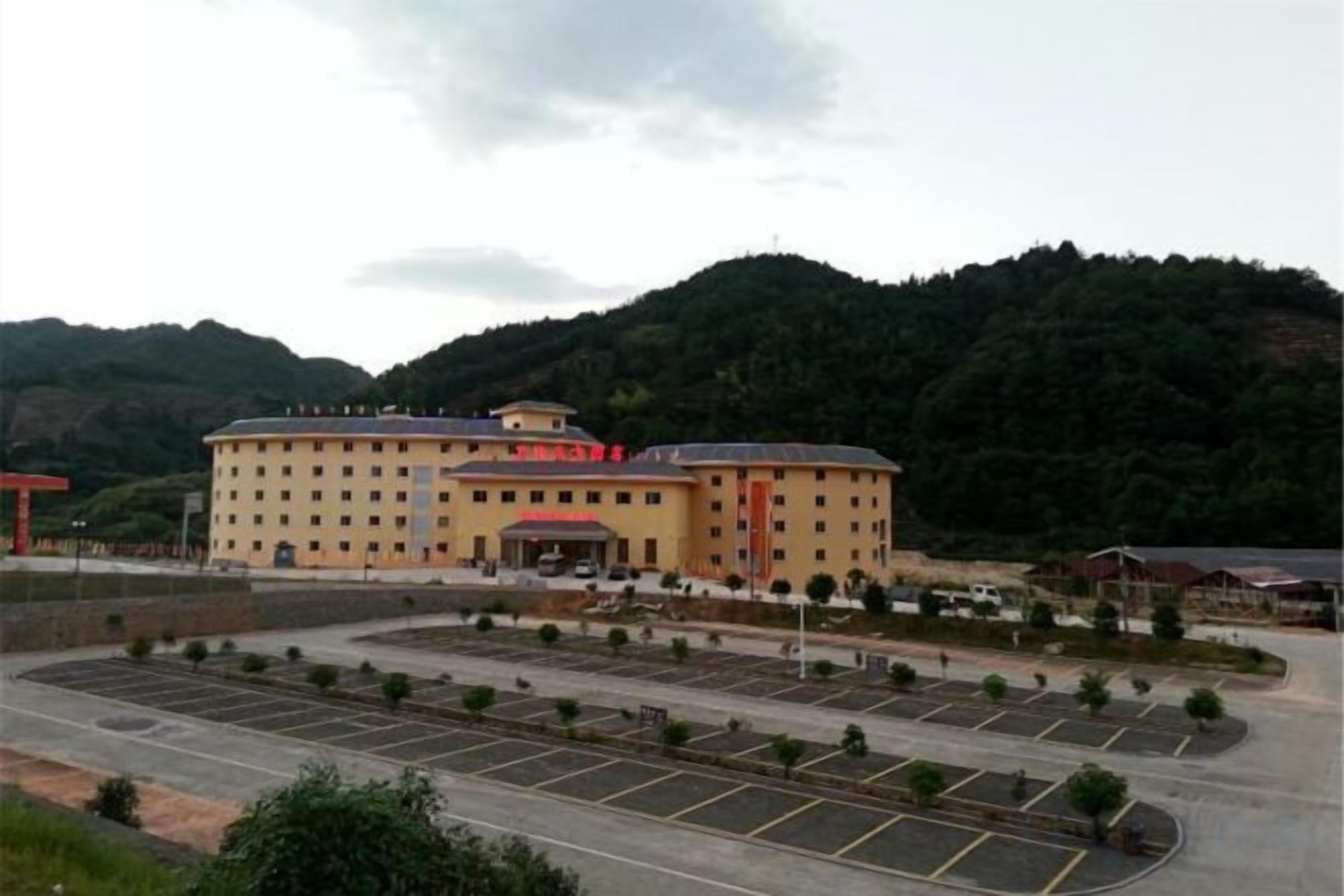 A large hotel with multiple floors, a parking lot, and a mountainous backdrop.