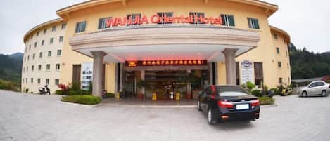 A hotel with a curved facade, a signboard with Chinese characters, and a car parked in front.