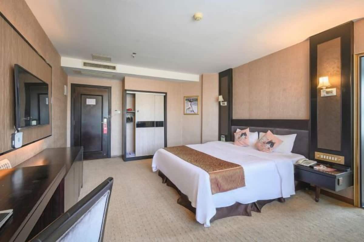 A hotel room with a large bed, a desk, a television, and a door leading to a bathroom.