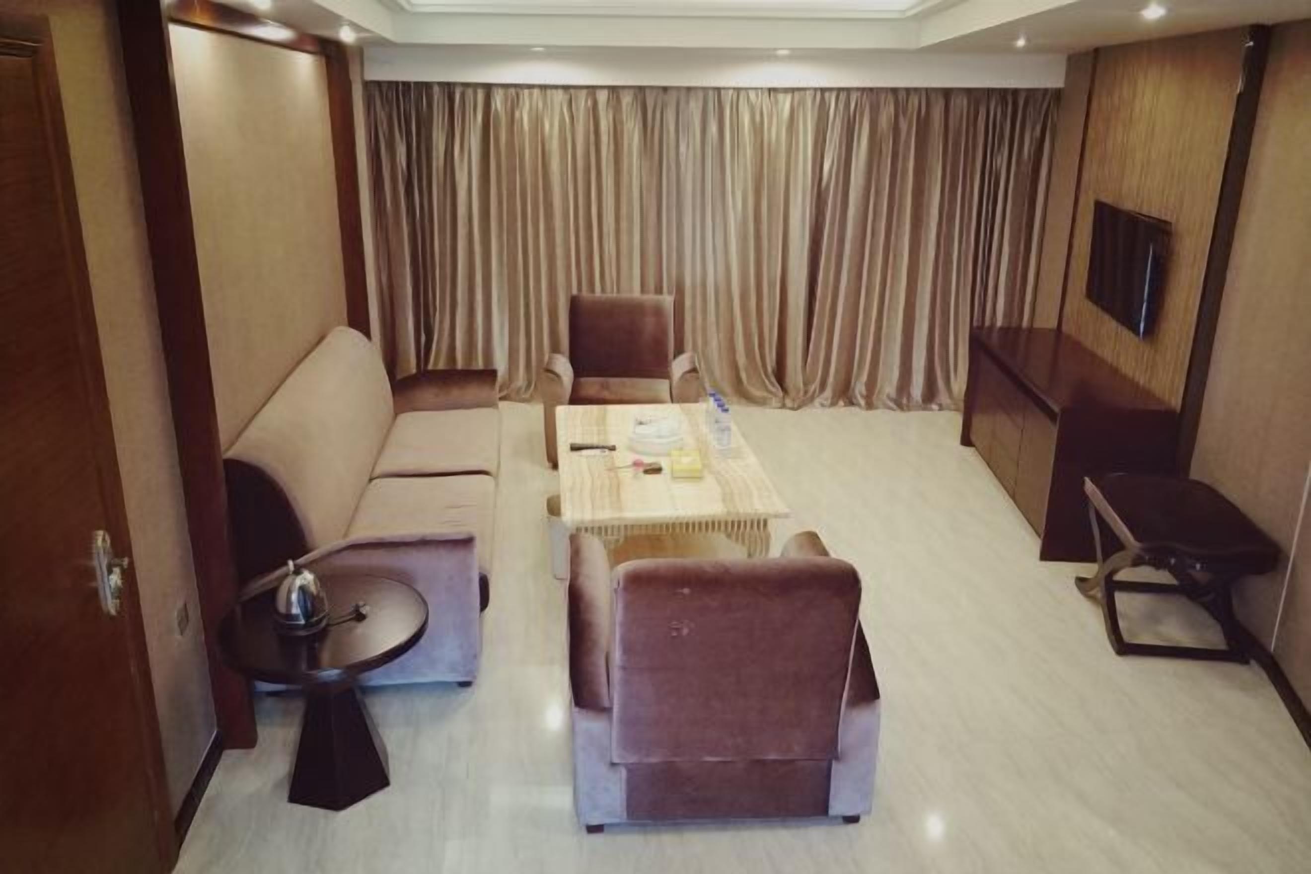 Une chambre d’hôtel équipée d’un canapé, de fauteuils, d’une table basse, d’un téléviseur et d’un rideau servant de décor.