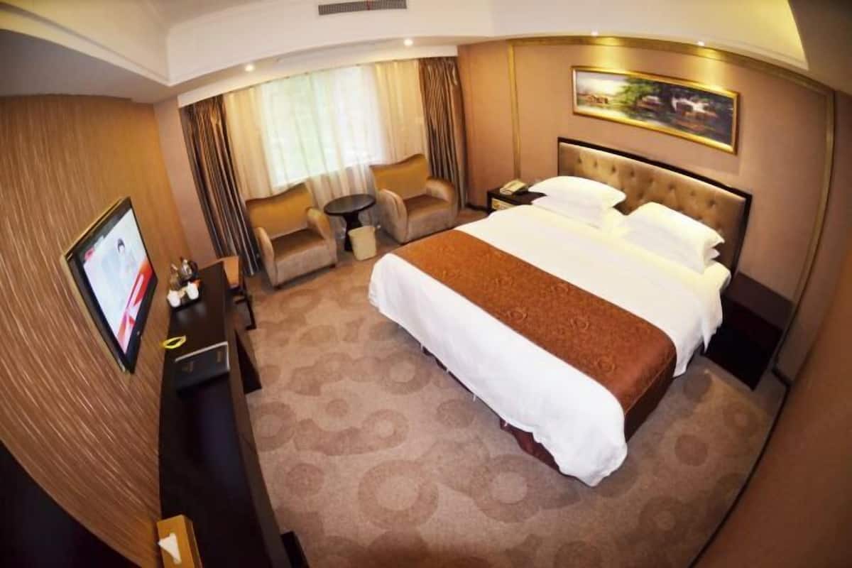 A hotel room with a large bed, a desk, a chair, and a television.