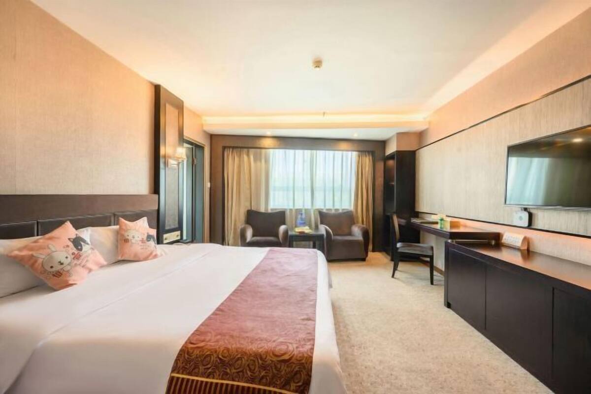 A hotel room with a large bed, a desk, a chair, a television, and a window with curtains.