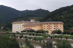 A large, multi-story building with a flat roof, surrounded by trees and hills.