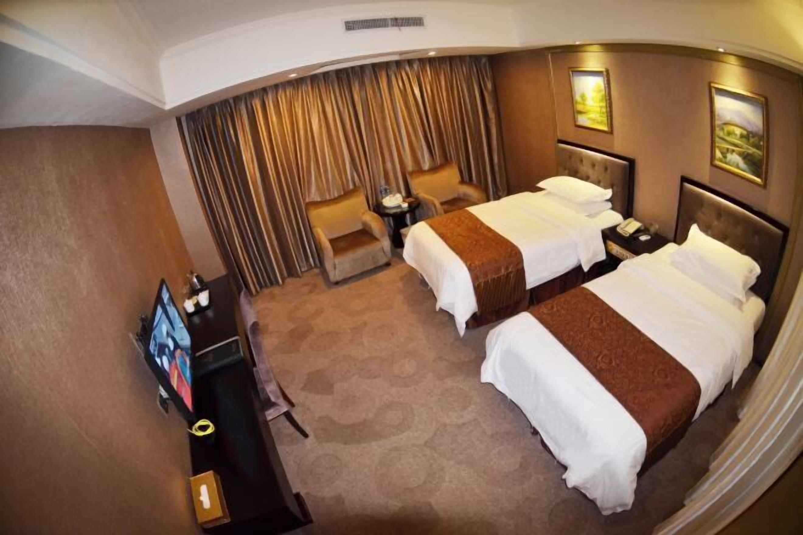 Une chambre d’hôtel avec deux lits, un bureau avec une télévision, une chaise et un rideau.