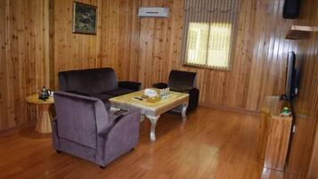 Una habitación con paneles de madera, un sofá, dos sillones, una mesita, un televisor y una ventana con cortinas.