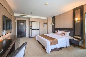 A hotel room with a bed, bedside table, TV, and a door leading to a bathroom. - Wanjia Oriental Hotel (Nanjing County)
