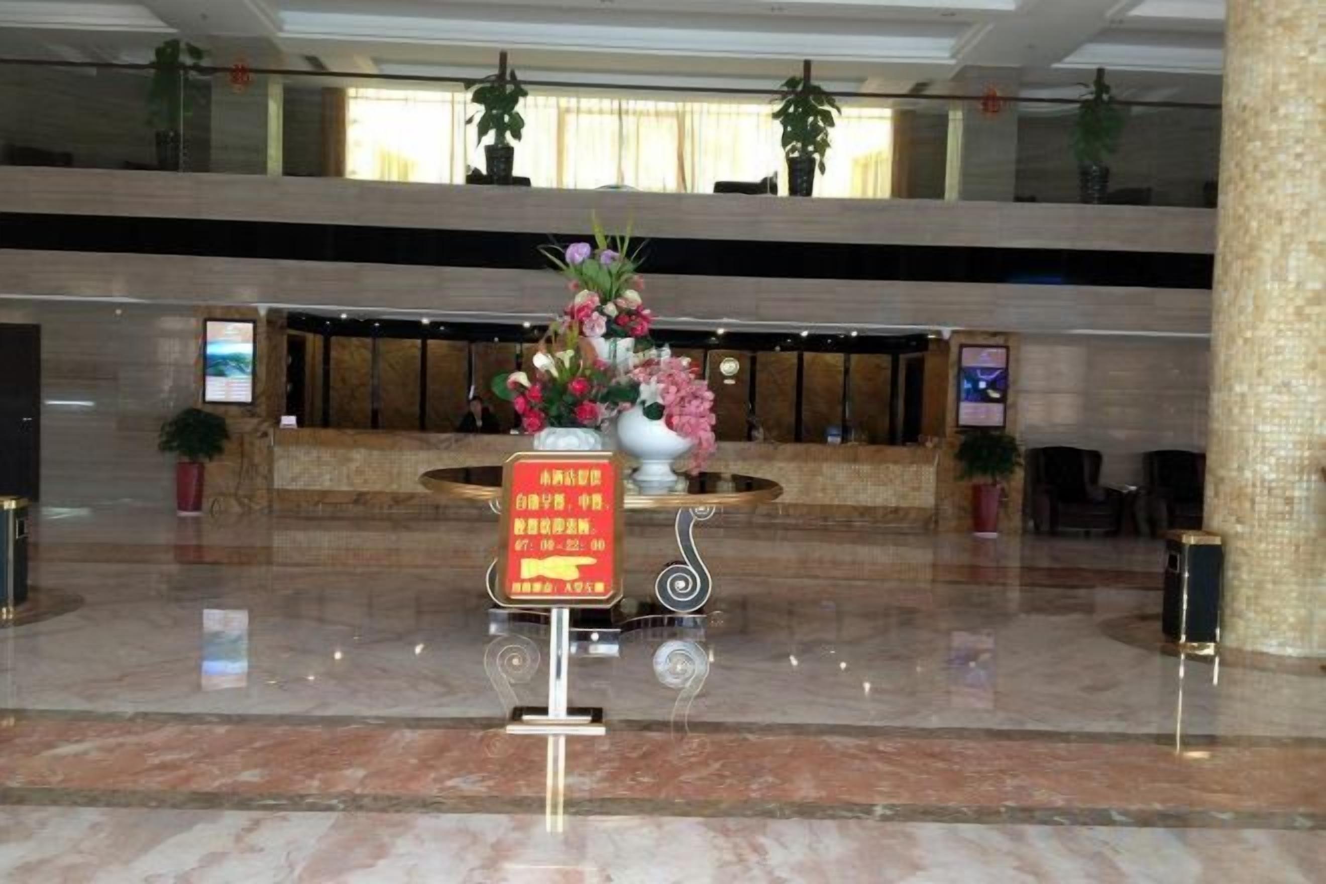 A hotel lobby with a reception desk, a large vase of flowers, and a sign with text.