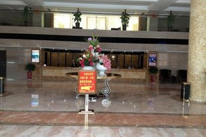 A hotel lobby with a reception desk, a large vase of flowers, and a sign with text. - Wanjia Oriental Hotel (Nanjing County)