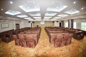 Un salón de conferencias con techo alto, varias mesas y sillas dispuestas para reuniones.