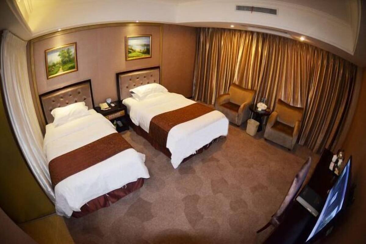 A hotel room with two beds, a TV, a chair, and a desk.