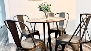 Un coin repas avec une table ronde et quatre chaises, une œuvre d’art représentant des feuilles encadrée au mur, et un vase avec des fleurs sur la table.