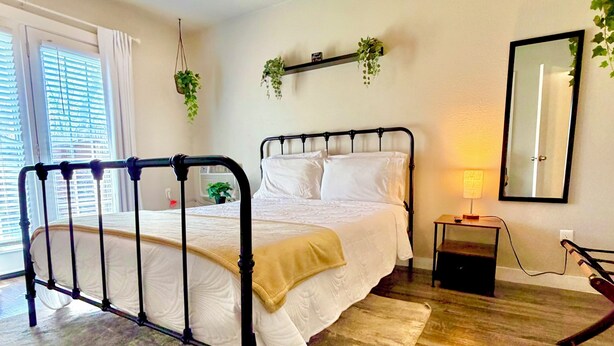 Une chambre à coucher comprenant un lit, un ventilateur de plafond, une table de chevet avec une lampe, un miroir et une fenêtre avec des stores.