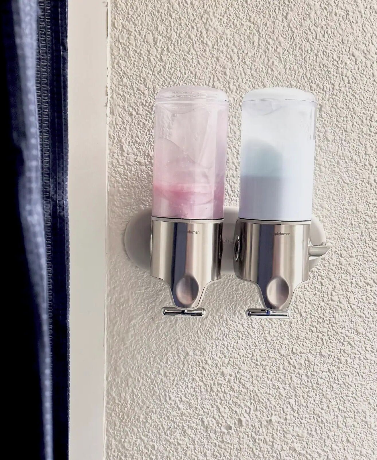 Zwei an der Wand befestigte Spender mit metallischem Fuß und durchsichtiger Füllung, vermutlich für Seife oder Lotion.