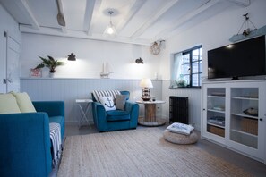 Una sala de estar con un sofá azul, una mesita con una lámpara, una estantería y un televisor.