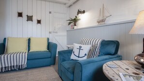 Una stanza accogliente con due divani blu, uno con cuscini gialli e l'altro con cuscini blu, un tavolino rotondo in legno e una decorazione a forma di nave fissata al muro.