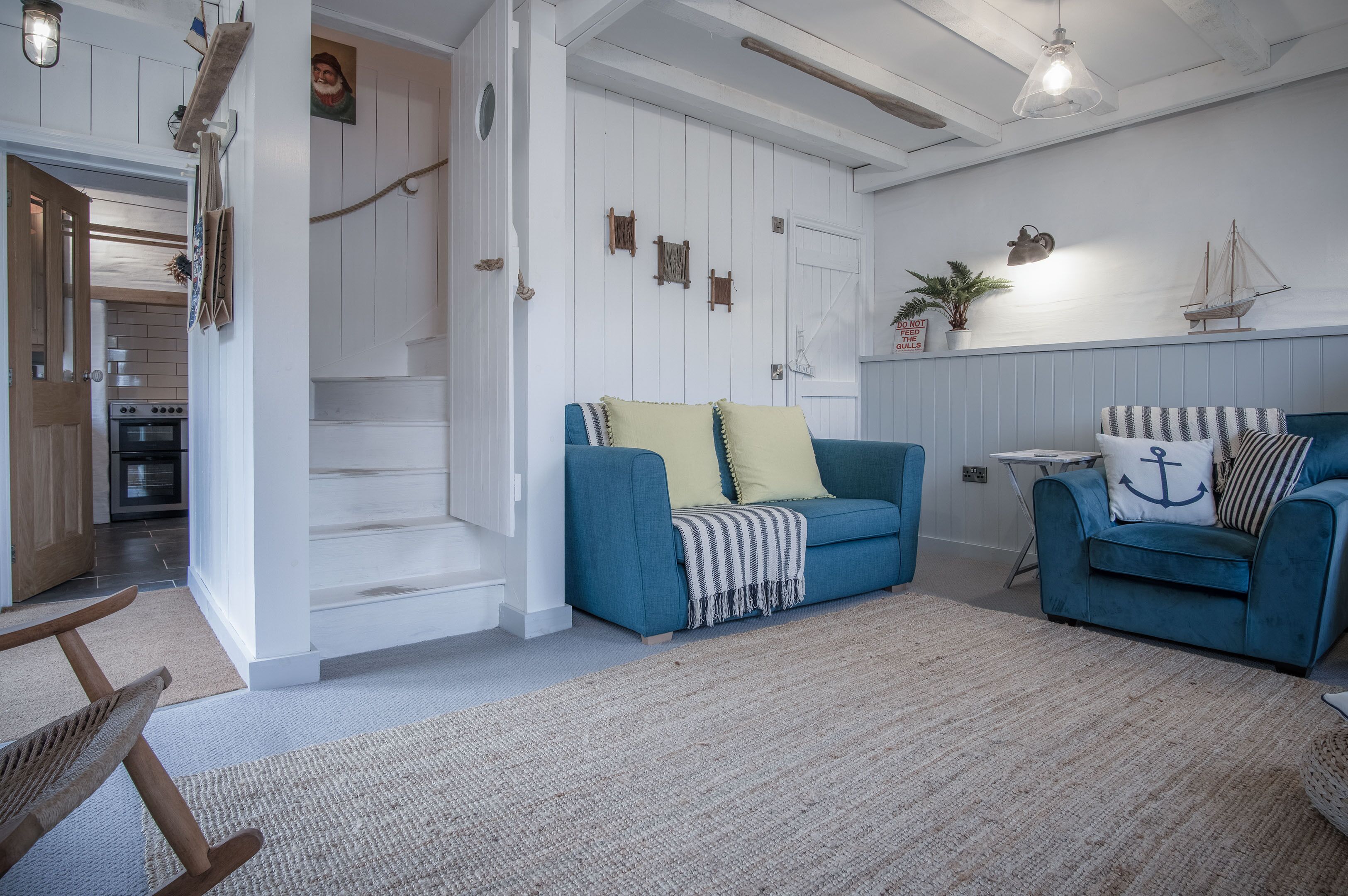 A living room with a blue sofa, a wooden rocking chair, and a staircase leading to another room.